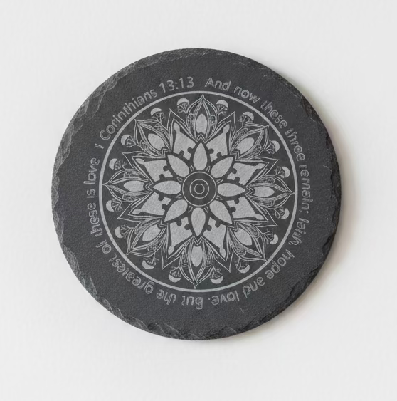 A round slate coaster featuring a white mandala design and the Bible verse Ephesians 2:14-15, displayed on a rustic wood slice background.